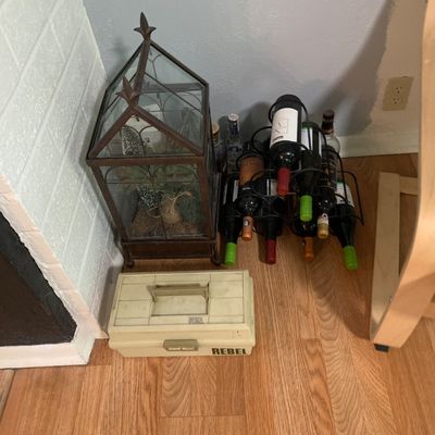 Sale Photo Thumbnail #60: Collection of floor items including a metal wire wine rack holding assorted bottles, a large metal architectural lantern terrarium, and a vintage Rebel plastic tackle box.