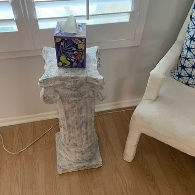 Sale Photo Thumbnail #7: Faux-stone Classical Ionic column pedestal stand with a distressed weathered finish, shown holding a tissue box next to an armchair.