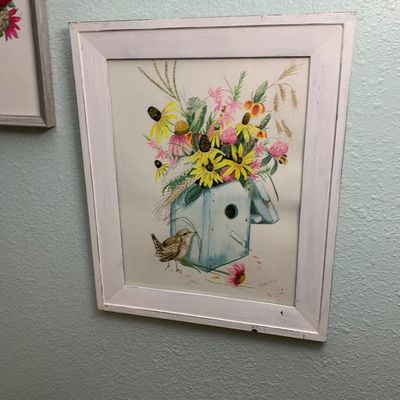 Sale Photo Thumbnail #121: Framed floral and bird art print featuring a blue birdhouse overflowing with wildflowers, set in a white wood frame.
