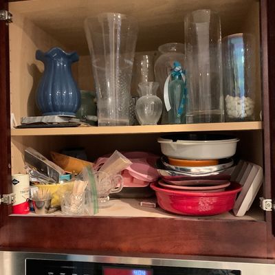 Sale Photo Thumbnail #18: Open kitchen cabinet filled with various glass vases, decorative pottery, baking pans, and miscellaneous kitchen smalls above a built-in oven.