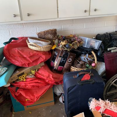 Sale Photo Thumbnail #47: Assorted household items, including a navy blue softside suitcase, boxed Keurig coffee maker, woven baskets, seasonal wreaths, and storage bags stacked beneath garage cabinets.