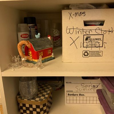 Sale Photo Thumbnail #99: White storage shelving filled with household items, including a barn-shaped teapot, clear acrylic deer figurines, spray paint, decorative boxes, and Bankers Box storage containers.
