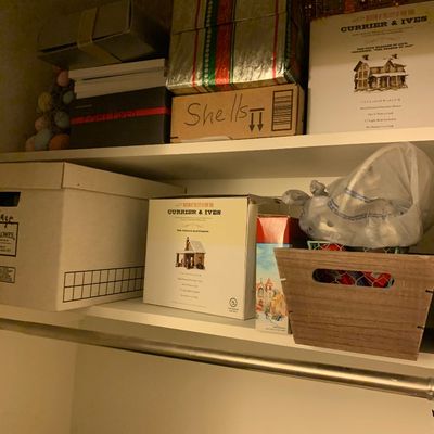 Sale Photo Thumbnail #101: Closet shelves stored with holiday decor, including boxed Currier & Ives porcelain village buildings, wrapped gift boxes, and a wooden tote bin.
