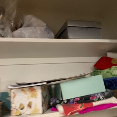 Sale Photo Thumbnail #117: Closet shelves stored with assorted items including a silver Nine West shoebox, decorative storage boxes, and folded colorful fabrics.