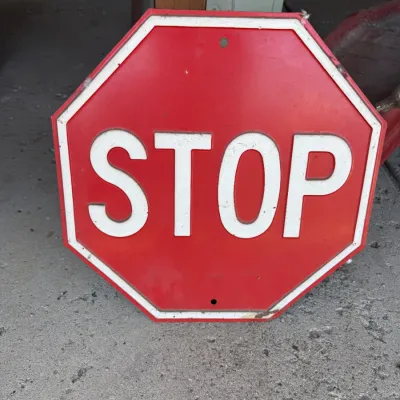 Vintage metal embossed red stop sign showing light wear, scuffs, and pre-drilled mounting holes.