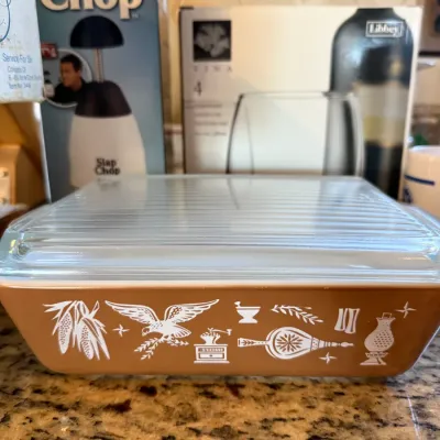 Sale Photo Thumbnail #31: Vintage Pyrex Early American pattern brown rectangular casserole dish with clear glass ribbed lid, sitting in front of boxed kitchen items.
