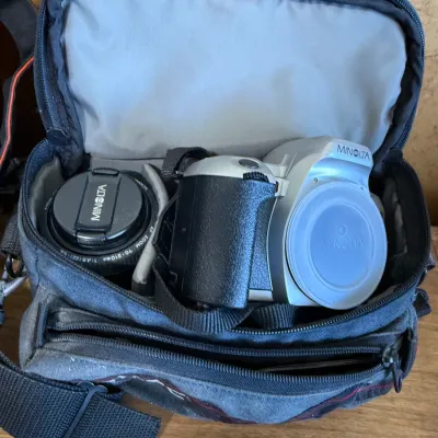 Minolta silver SLR camera body and a 70-210mm zoom lens, stored inside a padded fabric camera bag.