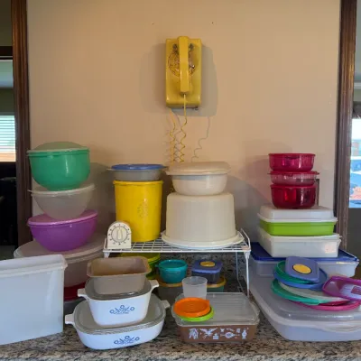 Large collection of vintage plastic Tupperware and Pyrex cookware, accompanied by a yellow wall-mounted rotary telephone.