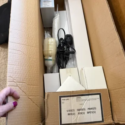 Cardboard box containing a studio lighting setup, including bulbs, cords, mounting hardware, and boxed components.