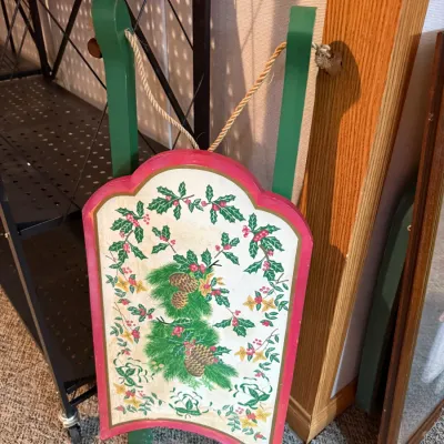 Sale Photo Thumbnail #25: Vintage painted wooden decorative Christmas sled featuring green runners, a red trim border, and a center panel decorated with pinecones, holly, and winter foliage.