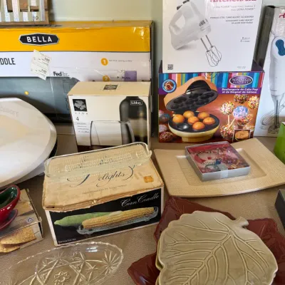 Assortment of boxed kitchen appliances and tableware, including a KitchenAid hand mixer, Nostalgia cake pop maker, clear glassware, and...