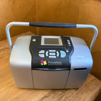 Epson PictureMate personal photo printer in silver and black, featuring a fold-down carrying handle and built-in LCD screen, circa 2000s.