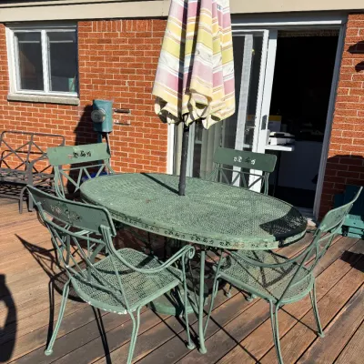 Sale Photo Thumbnail #46: Vintage green wrought iron patio set including an oval mesh-top dining table, four chairs with ivy details, and a striped market umbrella.
