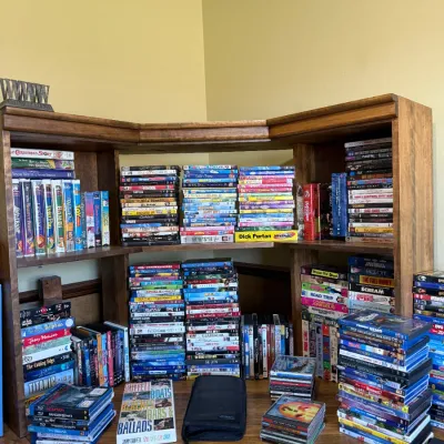 Large collection of DVDs, Blu-rays, and CDs arranged on a wooden corner hutch desk unit.