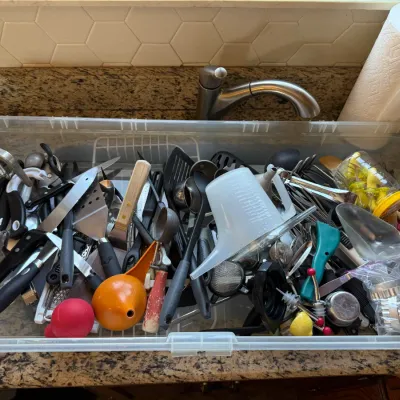 Large clear plastic storage bin filled with an assortment of vintage and modern kitchen utensils, including spatulas, measuring tools,...