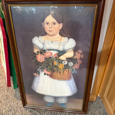 Sale Photo Thumbnail #24: Framed folk art style reproduction print depicting a young girl in a white dress holding a basket of flowers, set in a molded dark wood frame with gold inner trim.