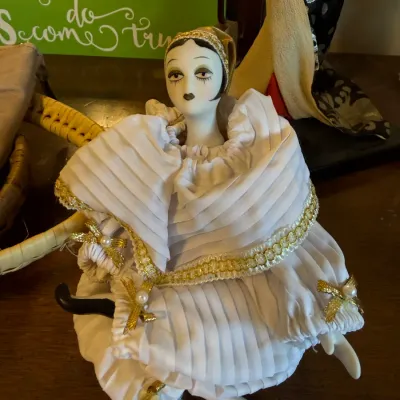 Vintage porcelain harlequin clown doll dressed in a ruffled white outfit with gold trim and faux pearl accents.