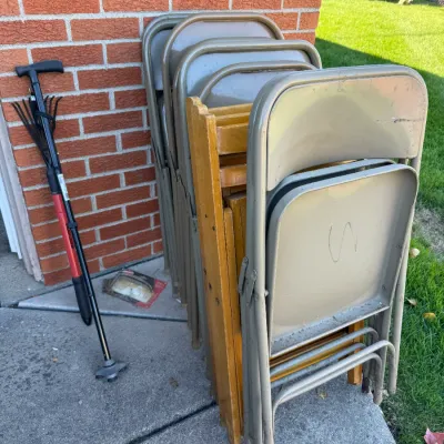 Sale Photo Thumbnail #44: Stack of vintage metal folding chairs alongside wooden folding chairs and a mobility cane against a brick wall.