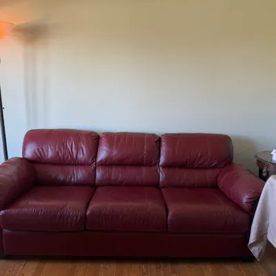 Burgundy leather three-cushion sofa flanked by a metal torchiere floor lamp and a small accent table.