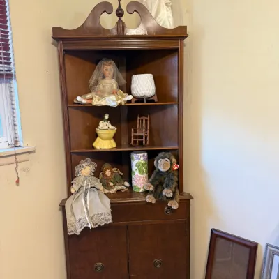 Vintage dark wood corner hutch with a broken pediment, featuring open shelves filled with collectible dolls, decor, and a Ty Beanie Baby...