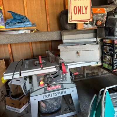 Sale Photo Thumbnail #39: Craftsman 3.0 HP table saw with stand, alongside a metal toolbox and various garage workshop items.