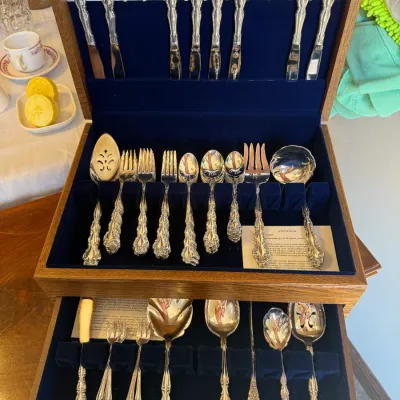Vintage ornate silver-plated flatware set housed in a two-tier wooden storage chest with a blue felt-lined interior.