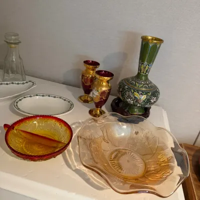 Sale Photo Thumbnail #23: Assortment of vintage glassware and decorative items, including a green cloisonné vase on a wooden stand, ruby red flashed small vases with gold embellishments, amber glass bowls, and porcelain dishes.