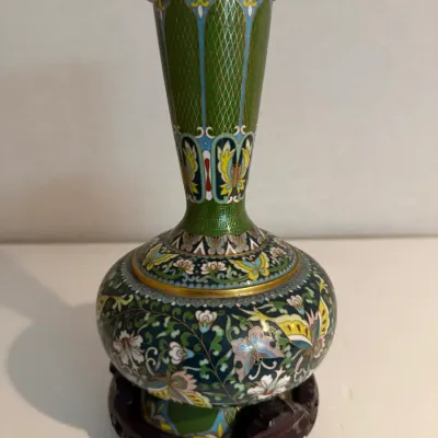 Sale Photo Thumbnail #14: Intricate cloisonné vase featuring colorful floral and butterfly motifs over a green and black enamel ground, complete with a fitted carved wooden base.