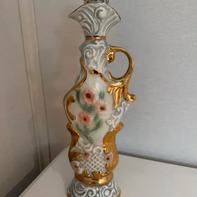 Sale Photo Thumbnail #12: Vintage ornate porcelain decanter featuring hand-painted floral motifs and heavy gilt scroll accents with a matching stopper.