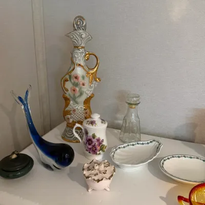 Sale Photo Thumbnail #33: Collection of vintage decorative glassware and porcelain items, including a blue art glass whale figure, a gilded decanter, floral lidded jars, and small trinket dishes.