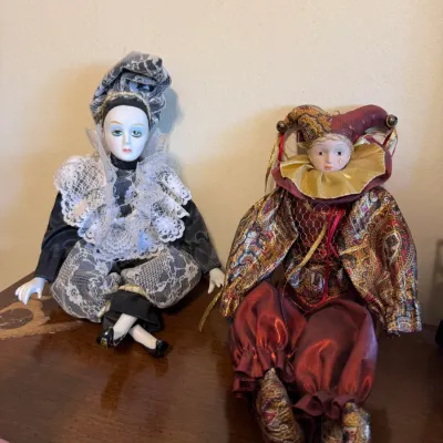 Pair of vintage porcelain jester and harlequin dolls featuring ornate fabric costumes with lace accents, metallic trim, and hand-painted...