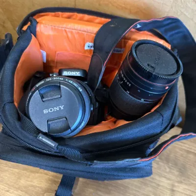 Sony DSLR camera body with a 100-300mm zoom lens attached and an additional lens stored inside a black and orange padded camera bag.