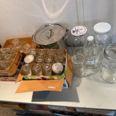 Sale Photo Thumbnail #26: Assortment of glass canning jars in cardboard boxes alongside large clear glass storage jars and a stainless steel stock pot.