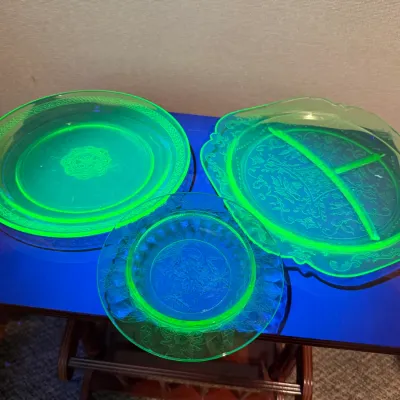 Sale Photo Thumbnail #32: Set of three vintage Depression-era green uranium glass plates glowing bright fluorescent under blacklight, featuring intricate floral and etched patterns.