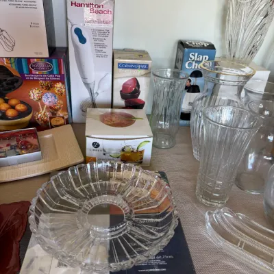 Collection of kitchenware and glassware, including boxed small appliances like a Hamilton Beach hand blender and Nostalgia Electrics cake...