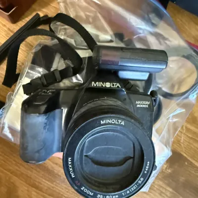 Minolta Maxxum 3000i 35mm SLR camera fitted with a Minolta Maxxum AF 35-80mm f/4-5.6 zoom lens, neck strap, and flash attachment, circa...