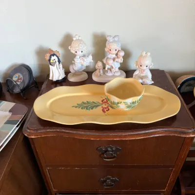 Collection of porcelain figurines, including Precious Moments, displayed alongside a yellow ceramic tray with matching dip bowl on a...