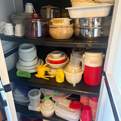 Sale Photo Thumbnail #78: Black plastic storage cabinet filled with kitchenware, including Pyrex mixing bowls, ceramic serving dishes, coffee mugs, a Coleman beverage jug, and food storage containers.