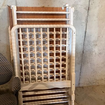Sale Photo Thumbnail #124: Disassembled vintage off-white wooden crib with spindle detailing, leaned against a concrete wall.