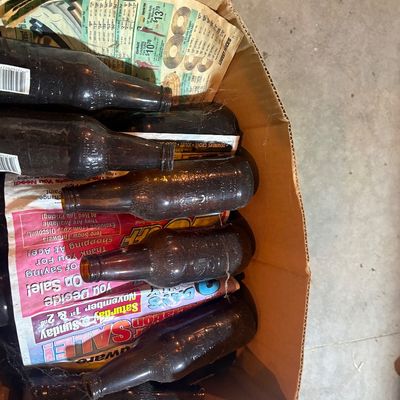 Sale Photo Thumbnail #88: Cardboard box containing a lot of vintage amber glass beer bottles wrapped in newspaper.