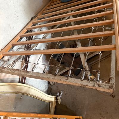 Sale Photo Thumbnail #106: Vintage metal spring bed frame support lying alongside wooden furniture components, showing surface wear and dust.