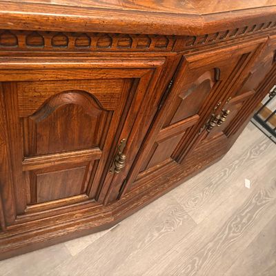 Sale Photo Thumbnail #2: Vintage dark oak sideboard featuring panel doors, carved detailing along the top trim, and decorative brass hardware.