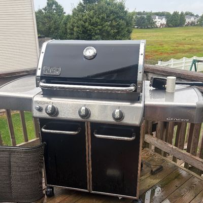 Sale Photo Thumbnail #14: Weber Genesis three-burner propane gas grill with a black porcelain-enameled lid, stainless steel side tables, and lower storage cabinet.