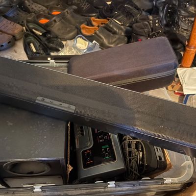 Sale Photo Thumbnail #71: Black soundbar speaker resting on top of various audio equipment and electronics inside a storage bin.