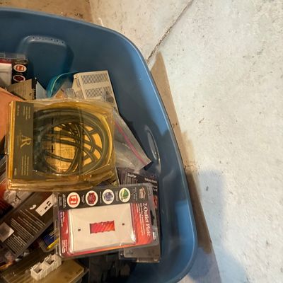 Sale Photo Thumbnail #109: Blue plastic storage bin filled with assorted packaged hardware and electrical supplies, including audio cables, outlet covers, and wall plates.
