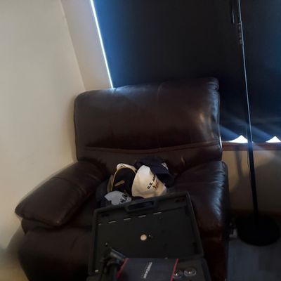 Sale Photo Thumbnail #10: Brown leather overstuffed recliner positioned in a living room near a window and floor lamp, with several U.S. Navy ball caps resting on the seat.