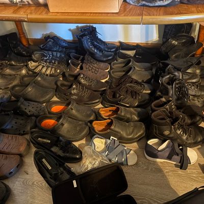 Sale Photo Thumbnail #72: Large collection of men's and women's shoes, work boots, Harley-Davidson riding boots, slip-ons, and clogs organized under a wooden table.