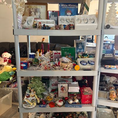 Sale Photo Thumbnail #58: Plastic shelving unit packed with holiday decorations, including boxed porcelain ornaments, Christmas figurines, plush toys, light sets, and winter-themed knick-knacks.