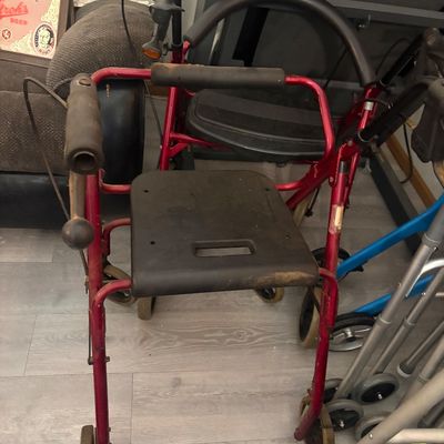 Sale Photo Thumbnail #25: Red four-wheeled rollator walker with a padded seat and hand brakes, showing signs of heavy use.