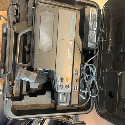 Sale Photo Thumbnail #61: Vintage Realistic Model 100 MovieCorder VHS camcorder housed in a black hard shell carrying case with original AC power adapter.